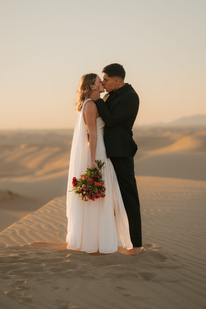 just married couple kisses on the top of a sand dune at the imperial glamis sand dunes during their elopement session at sunrise