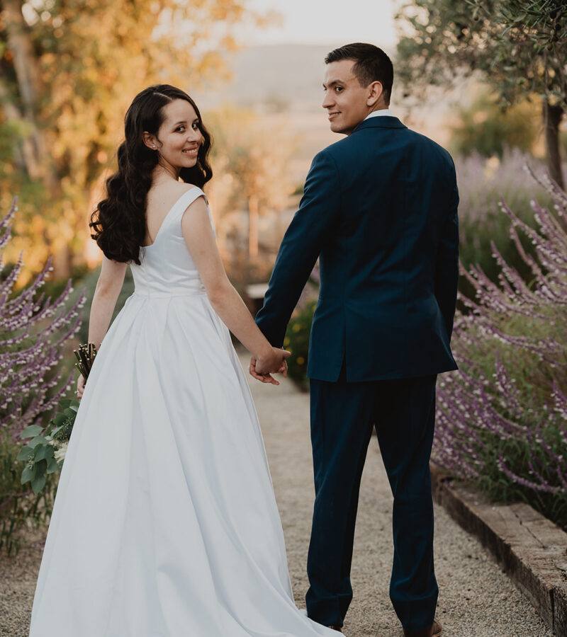 bride and groom look back at the camera and smile while holding hands at their wedding in ramona ca at lavender and olive venue
