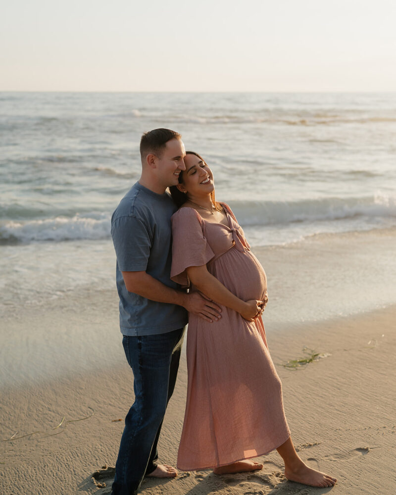 dad hugs pregnant expecting mom from behind during their sunset maternity beach session in la jolla