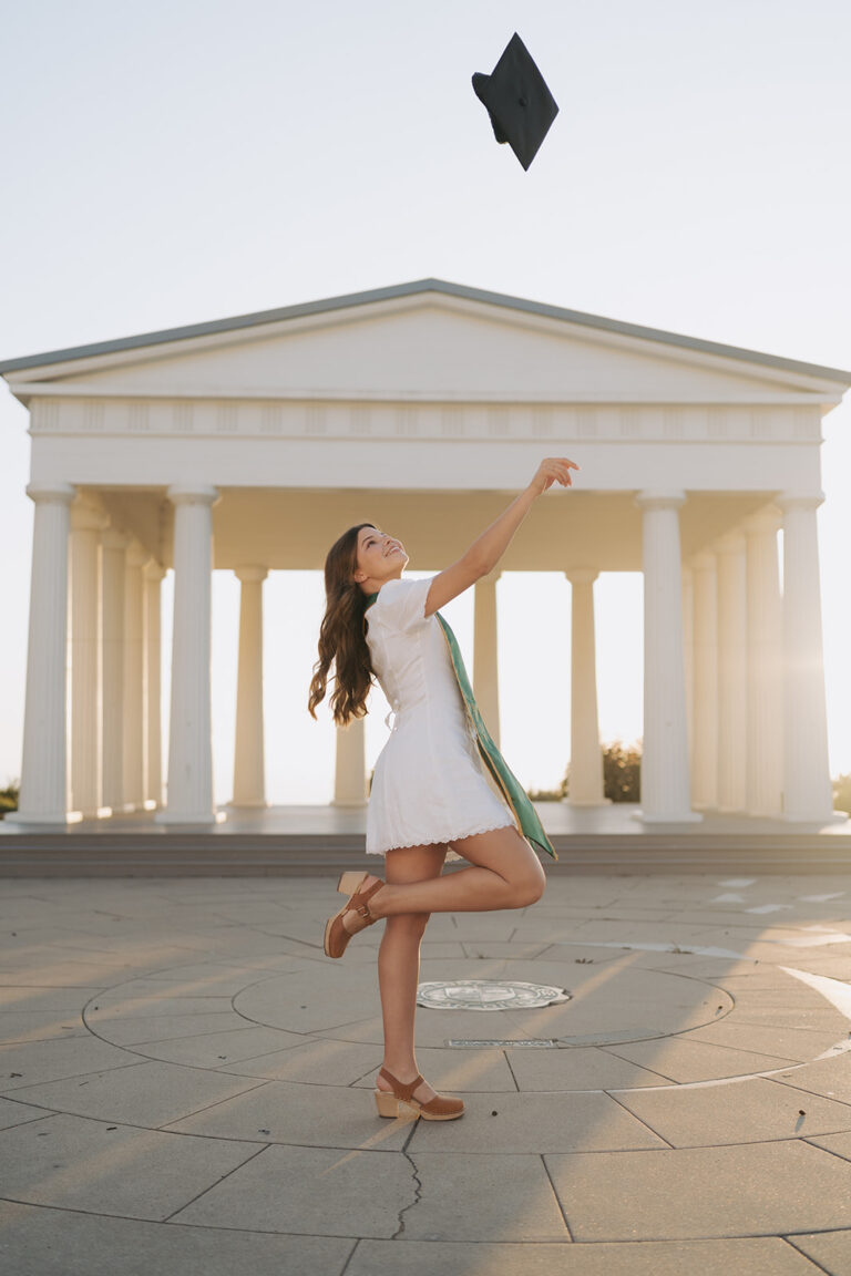 PLNU Grad photos College Senior Graduate throwing her cap in the air while standing in front of the Point Loma Nazarene Greek Amphitheater