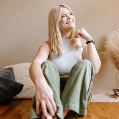 Photographer Alaina Yard of Alaina Yard photography smiles at the camera while sitting on the floor of a studio with various props behind her