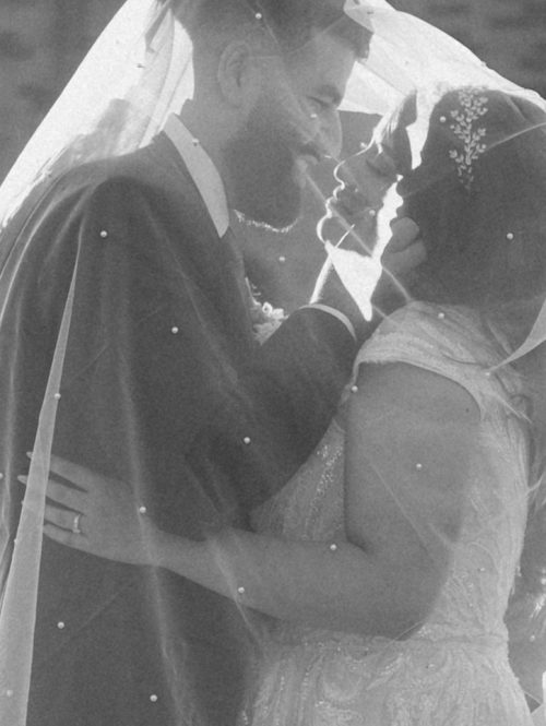 Bride and groom kiss under veil during golden hour wedding portraits